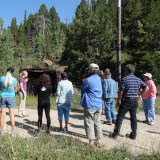 A group of people listening to a guide in front of a mine tunnel.