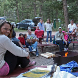 Group of people sitting on picnic tables around a campfire.
