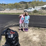 Two young children pose in front of bagged trash. They have Earth Day shirts on.