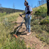 Woman is using a weed whip t clear weeds along a trail