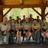 11 smiling rangers in uniform under a picnic shelter