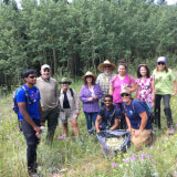 Photo of happy volunteers at the end of a weed pulling project with a bag full of weeds in front