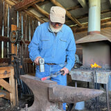 Blacksmith holding a hammer in one hand and hot steel with tongs in the other hand at anvil