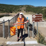 Woman in an orange vest standing with litter pickup supplies.