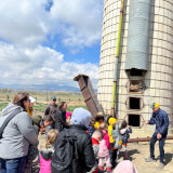 A volunteer tour guide shares stories with a class of students in front of a silo