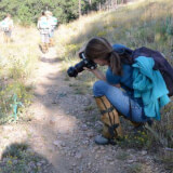 Woman taking a photo of a plant on a hiking trail. 