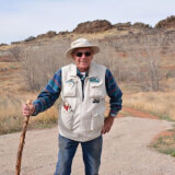 Man standing at a trailhead leaning on a walking stick. 