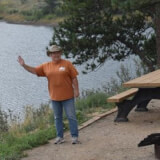 Woman standing in a campsite waving at the camera.